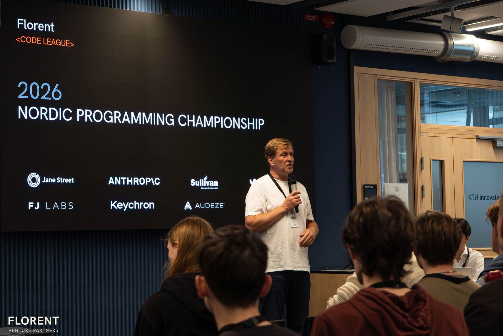 Speaker on stage in front of the 2026 Nordic Programming Championship screen and sponsor logos